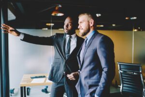 African american buisnessman pointing and standing near window with colleague talking about future plans.